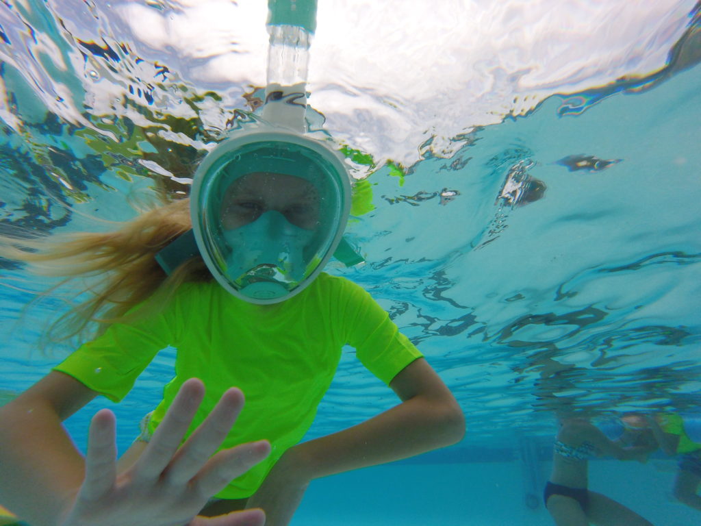 girl in mask swimming in pool waving